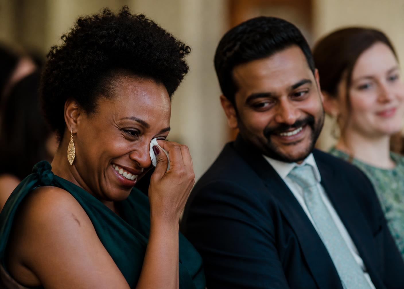 Wedding guests listening to a speech, one laughing through happy tears