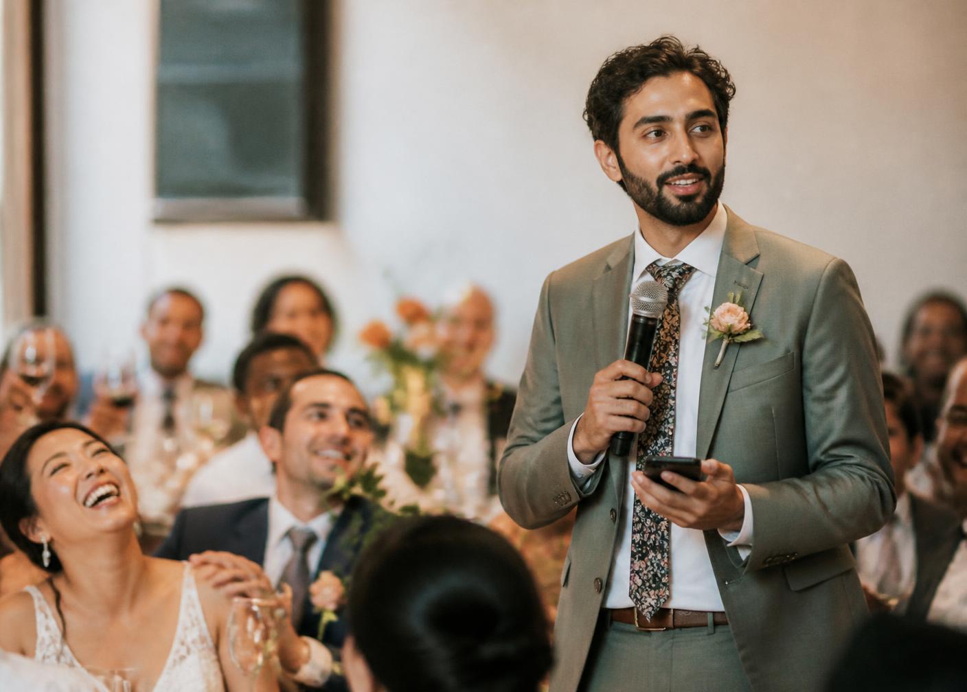 A wedding speaker delivering a toast with his notes in hand as guests smile